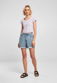 Levandulový krátký rukáv crop top s kulatým výstřihem a zapínáním na knoflíky, v kombinaci s světle modrými džíny s ohrnutými lemy. Černé sandály.