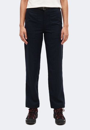 Personne portant un pantalon noir droit avec des poches plaquées à l'avant, une ceinture noire, une chemise blanche et des chaussures de randonnée noires avec des lacets rouges.