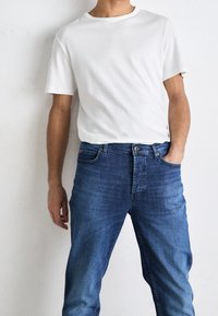 Biały bawełniany t-shirt z krótkimi rękawami, zestawiony z niebieskimi dżinsami o klasycznym kroju i delikatnym przetarciu.