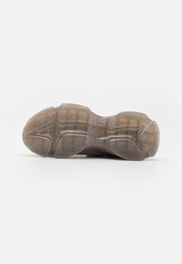 Translucente Gummisohle des Sneakers mit strukturiertem Zickzackmuster; abgerundete Form mit verstärkten Kanten; beige und graue Farbgestaltung.