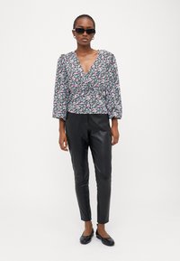 Blusa com estampado floral, decote em V, mangas longas bufantes e base preta. Combinada com calças de pele pretas e sapatos pretos planos. Modelo a usar óculos de sol.