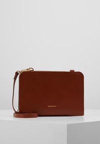 Braune Leder-Umhängetasche mit minimalistischem rechteckigem Design, goldfarbenem Logo, dünnem Schulterriemen und Reißverschluss.