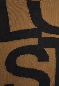 Stickad tröja med en svart grafisk design mot en senapsgul bakgrund, som visar en mjuk textur med djärva färgblock.