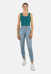 Teal kurzes Tanktop, hellblaue schmale Jeans mit hoher Taille und weiße Sneakers. Das Tanktop hat breite Träger und eine glatte Textur.