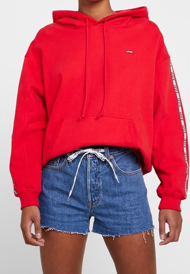 Red hooded sweatshirt with a front pocket and drawstrings, paired with blue denim shorts featuring frayed edges and a patterned waistband.
