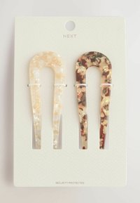 To hårklemmer: den ene er gennemsigtig beige med en marmoreret tekstur, den anden har et brunt og cremefarvet skildpaddeskal-mønster. Fastgjort til et baggrundskort.