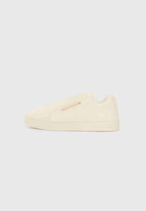 Sneakers slip-on beige con una texture liscia, caratterizzati da un logo in rilievo e un design minimalista. Suola in gomma spessa per supporto.