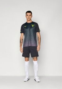 Juoda ir mėlynos spalvos gradientu futbolo marškinėliai su geltonais akcentais, juodi šortai, balti kojinės ir juodi sportbačiai su irkliais. Ant krūtinės yra logotipas.