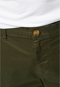 Pantaloni din bumbac de culoare verde măsliniu cu o textură netedă, având un sistem de închidere cu un buton maro și cusături în contrast pe căptușeală.