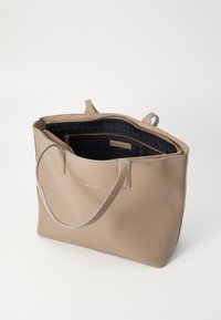 Sac fourre-tout en cuir beige avec une texture lisse, de doubles poignées, une fermeture éclair, et un intérieur doublé noir comprenant une poche zippée et un détail de marque.