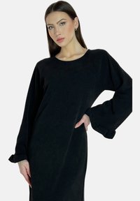 Robe noire à manches longues avec un col rond, dotée de manches évasées aux poignets volants et d'une coupe décontractée. Tissu doux et texturé.