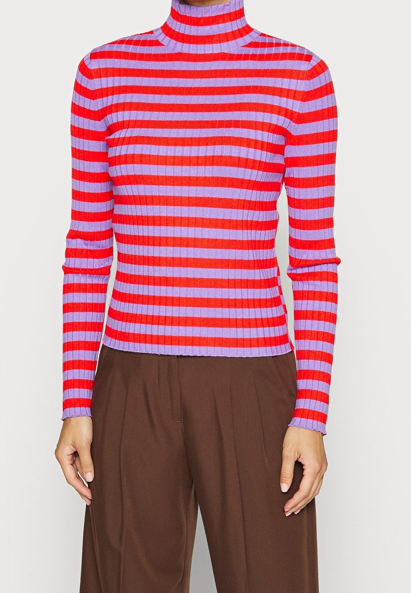 Tätt ribbad polotröja med horisontella röda och lila ränder, i kombination med lösa bruna byxor.