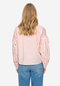 Hvid stribet bluse med røde lodrette linjer, puffede ærmer og afrundet kant. Kombineret med lyseblå denimjeans.