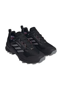 Czarne buty sportowe z siateczkową cholewką, skośną gumową podeszwą i trzema szarymi paskami. Szara podeszwa z teksturowanym gripem, akcentowana czerwonymi detalami.