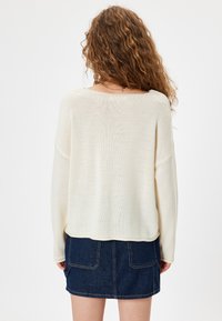 Maglione beige oversize con una vestibilità ampia e polsini a coste, abbinato a una mini gonna in denim scuro con due tasche posteriori.