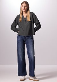 Blusa grigia scura a maniche lunghe con scollo a V e bottoni, abbinata a jeans in denim blu larghi e sneaker bianche. Design e texture semplici.