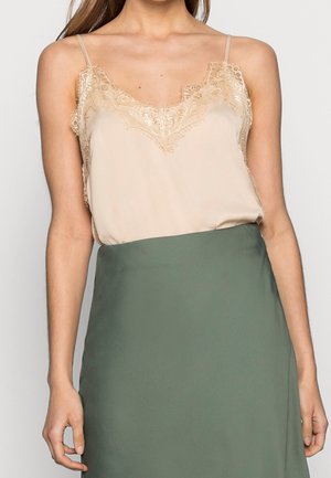 Woman wearing a beige lace-trimmed camisole tucked into a high-waisted olive green skirt, standing against a plain background.