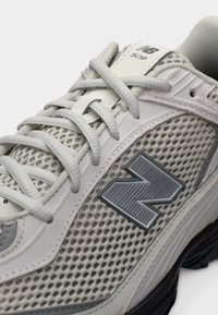 Gros plan d'une basket New Balance 508 gris clair avec tissu en mesh, lacets et un grand logo "N" sur le côté.