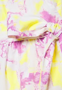 Tessuto bianco con vivaci motivi marmorizzati rosa e gialli, caratterizzato da un dettagliato fiocco annodato e una texture arricciata per un aspetto aderente.
