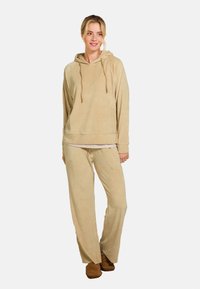 Beige hoodie met een ontspannen pasvorm en trekkoorden, gecombineerd met bijpassende brede joggingbroek in een zachte, gestructureerde stof.