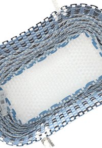 Cesto da viaggio intrecciato con materiali blu, neri e bianchi; forma rettangolare con un interno testurizzato e manici a contrasto.
