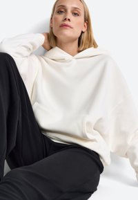 Kreemit värvi kapuutsiga särk, mis on valmistatud pehmest kangast, sisaldab pingutustrossiga kapuutsi ja esist kotti. Kombineeritud lõdva musta püksiga, et saavutada mugav välimus.