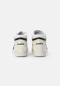Baskets montantes en cuir blanc avec des accents noirs, semelle en caoutchouc texturé et logo sur le talon. Lignes épurées et finition lisse.