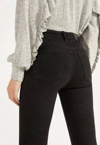 Svarta högmidjade jeans i denim, med två bakfickor och en slät yta. Matchat med en ljusgrå, volangtröja.