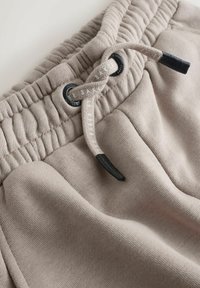 Light beige sweatpants with elastic waistband, drawstring, and black accents. Material appears soft with a smooth texture.