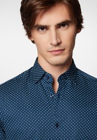 Niebieska koszula w wzór w diamenty, z kołnierzykiem na guziki i ciemnymi guzikami. Gładki materiał z subtelnym połyskiem.