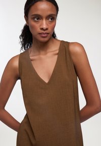 Abito brown senza maniche con scollo a V, realizzato in tessuto testurizzato e dal fit rilassato, caratterizzato da spalline larghe e dettagli di cucitura discreti.