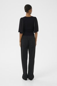 Top negru cu mâneci bufante, purtat împreună cu blugi negri cu talie înaltă. Textură fină, corset ajustat și design lejer al picioarelor cu buzunare.