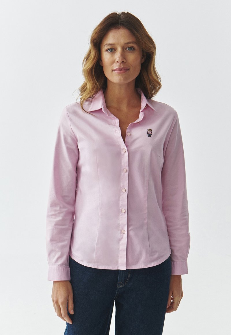 Camicia button-up rosa chiaro con maniche lunghe, caratterizzata da un piccolo ricamo di un orsetto sul petto, realizzata in un tessuto morbido.