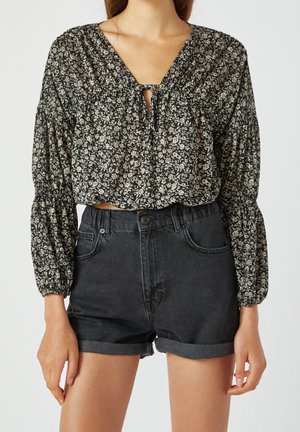 Woman wearing black floral long-sleeve blouse with keyhole neckline paired with rolled black denim shorts.