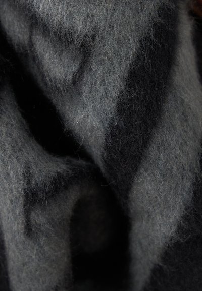 Gros plan d’un tissu en laine doux gris foncé avec des fibres fines visibles et des plis texturés créant ombres et lumières.