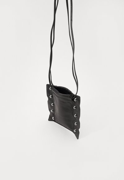 Black leather crossbody bag with scalloped edges, silver grommet accents, and two thin straps. Simple, rectangular design.