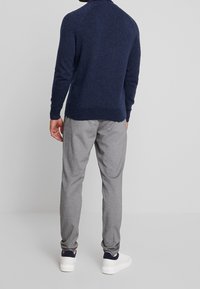Pull en maille bleu marine avec une finition texturée, associé à un pantalon de jogging gris clair et des baskets blanches. Accent sur le confort et le style décontracté.