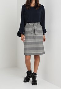 Maglietta a maniche lunghe blu navy, gonna a tubino grigia a quadri con dettagli alla vita e stivali neri alla caviglia con lacci e fibbie. Texture del tessuto morbide.