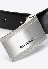 Metalen zilveren geldclip met een gestructureerd gripgedeelte en gegraveerd "WITTCHEN"-logo, bevestigd aan een zwarte leren riem.