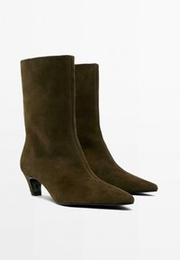 Stivaletti alla caviglia in suede marrone con silhouette aderente, punta appuntita e tacco basso a blocco. Texture liscia con dettagli minimi.
