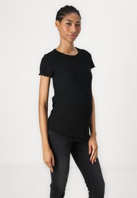 Svart ribbet kortermet topp med en tett design og bølgete kanter, paret med mørke jeans, vist på en modell mot en hvit bakgrunn.