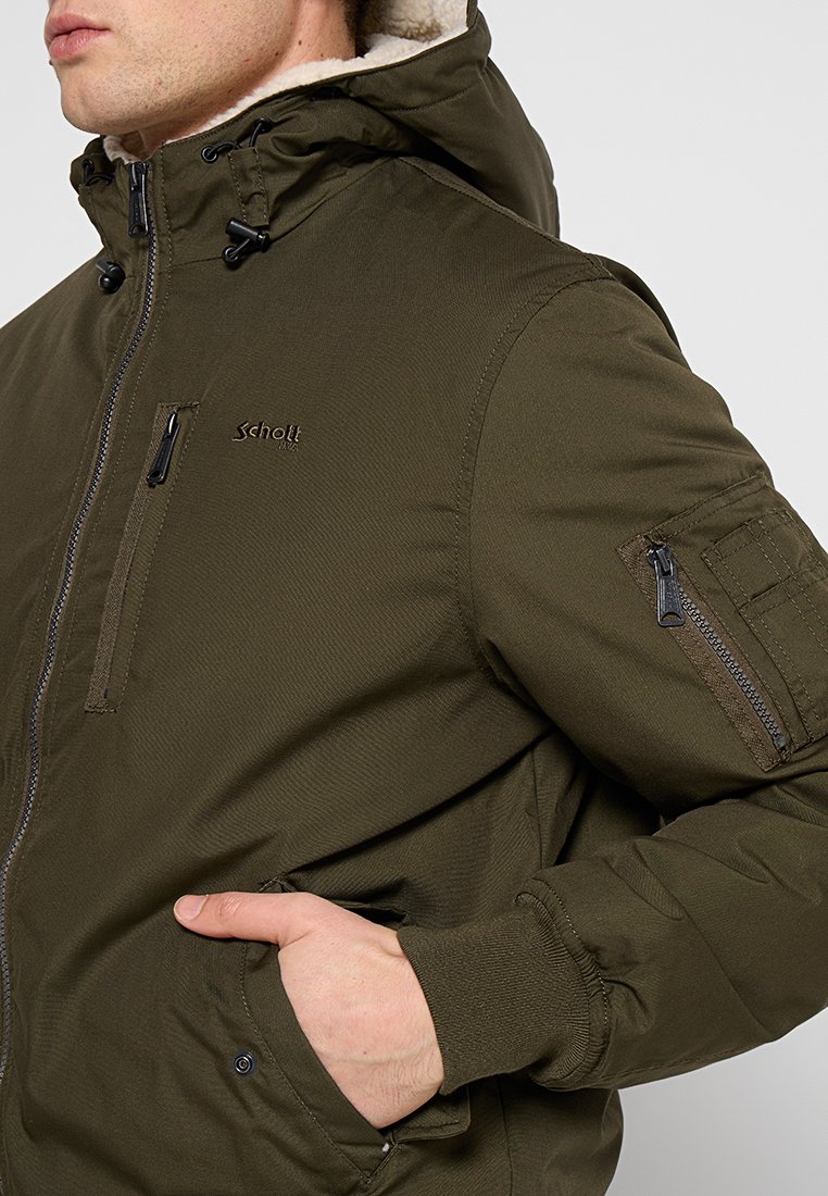 Veste bomber khaki avec une capuche zippée, des poches avant et une poche latérale. Elle possède une doublure intérieure douce et un extérieur texturé.