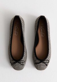 Scarpe basse in bianco e nero con un design tessuto testurizzato, punta arrotondata, bordi neri e un piccolo fiocco decorativo sulla parte anteriore. Interno a calzata ampia.