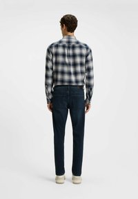 Camisa de franela a cuadros en tonos de azul marino y blanco, combinada con jeans de denim oscuro. Presenta un cuello clásico y mangas largas.