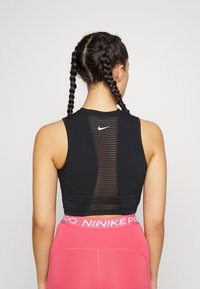 Sort ærmeløs cropped top med et netpanel på ryggen, der har en lille hvid Nike-logo. Kombineret med rosa leggings med høj talje.