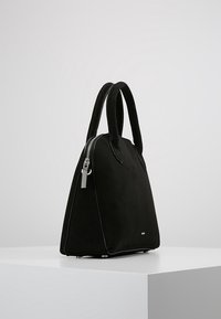 Černá semišová kabelka se strukturovaným tvarem, dvojitými rukojeťmi, bočním zipem a lesklými stříbrnými kovovými doplňky. Hladký povrch bez viditelných vzorů.