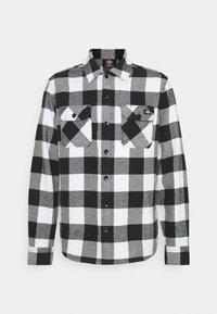 Chemise en flanelle à carreaux noir et blanc avec un devant boutonné, deux poches poitrine avec rabats à boutons, et un col pointu.