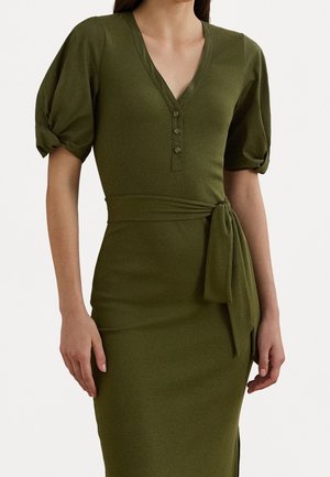 Vestido ajustado verde oliva con escote en V, tres botones, mangas cortas abullonadas y cinturón anudado en la cintura sobre una mujer de pie.