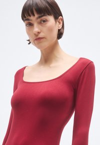 Burgundské body s dlhými rukávmi, štvorcovým výstrihom a hladkou textúrou, zdôrazňujúce priliehavú siluetu. Minimalistický dizajn, bez vzorov.