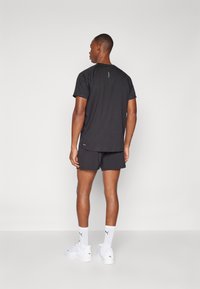 Svart tränings t-shirt med korta ärmar, slät textur och en liten accent på baksidan; kombinerad med svarta shorts och vita sneakers.